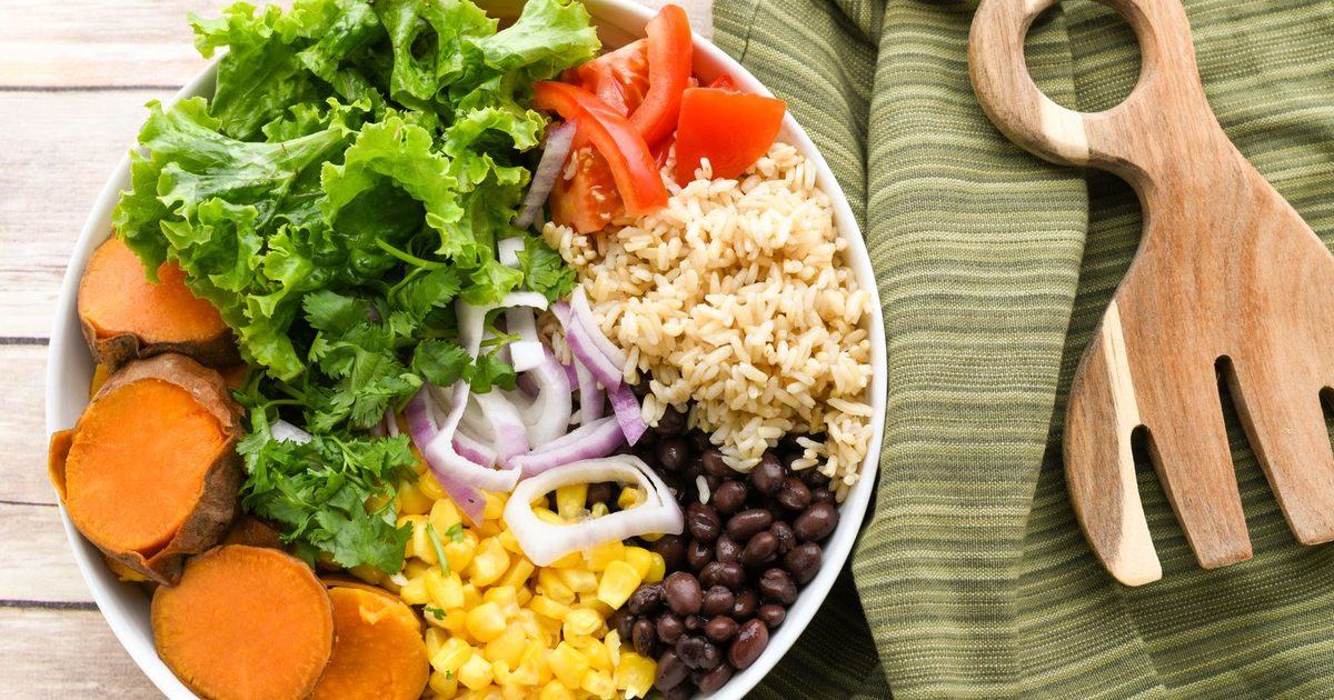 A buddha bowl with fresh vegetables, rice and beans on a wooden table