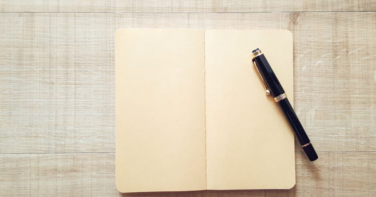An open notebook with a pen resting on it on a wooden surface