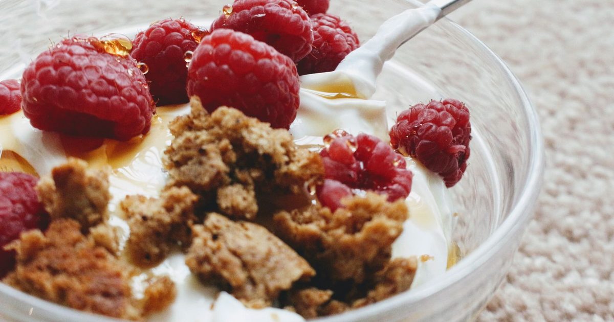 A bowl of yoghurt topped with fresh raspberries and biscuit crumb